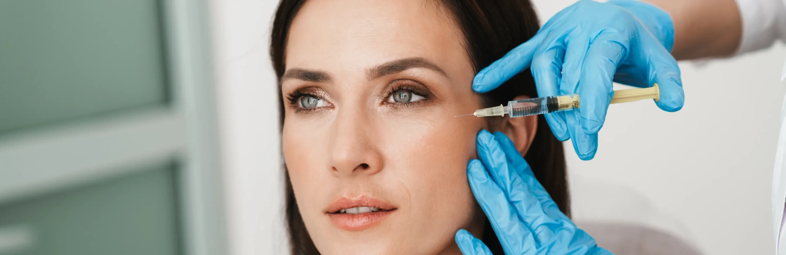 Woman receiving a cosmetic facial injection near the eye area from a professional wearing blue gloves.